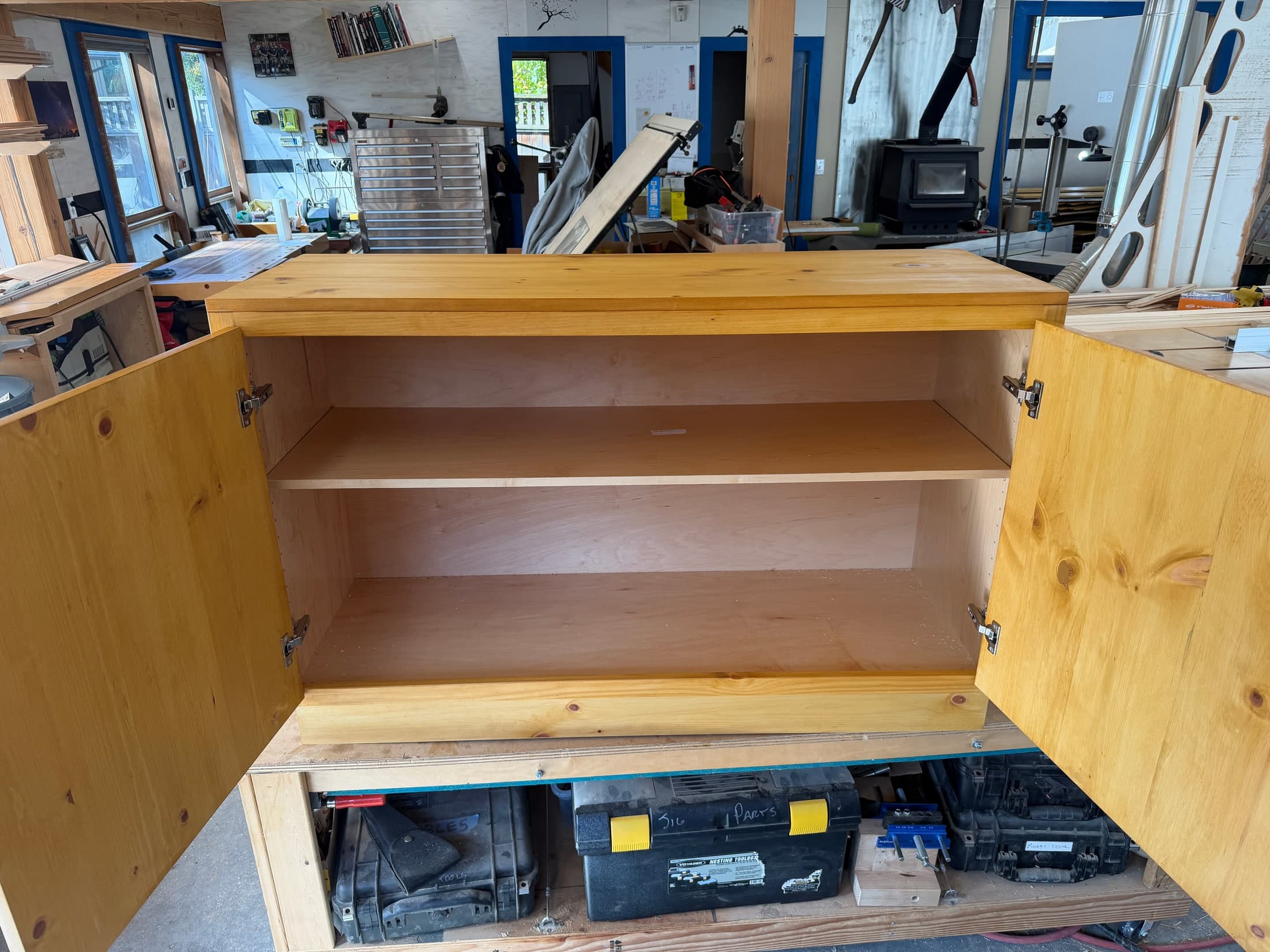 Pine base cabinet on the shop bench with both solid pine doors open, showing the plywood interior and shelf