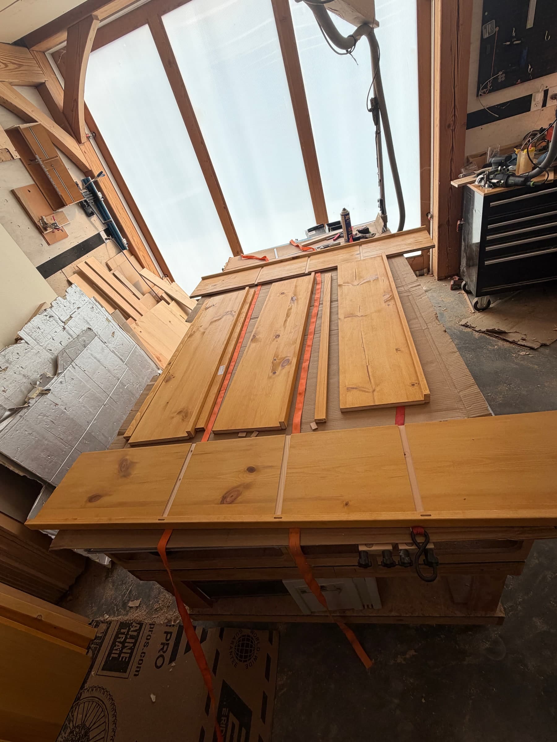 Pine shelf parts and solid wood stiffeners laid out on the shop bench with orange ratchet straps during glue-up