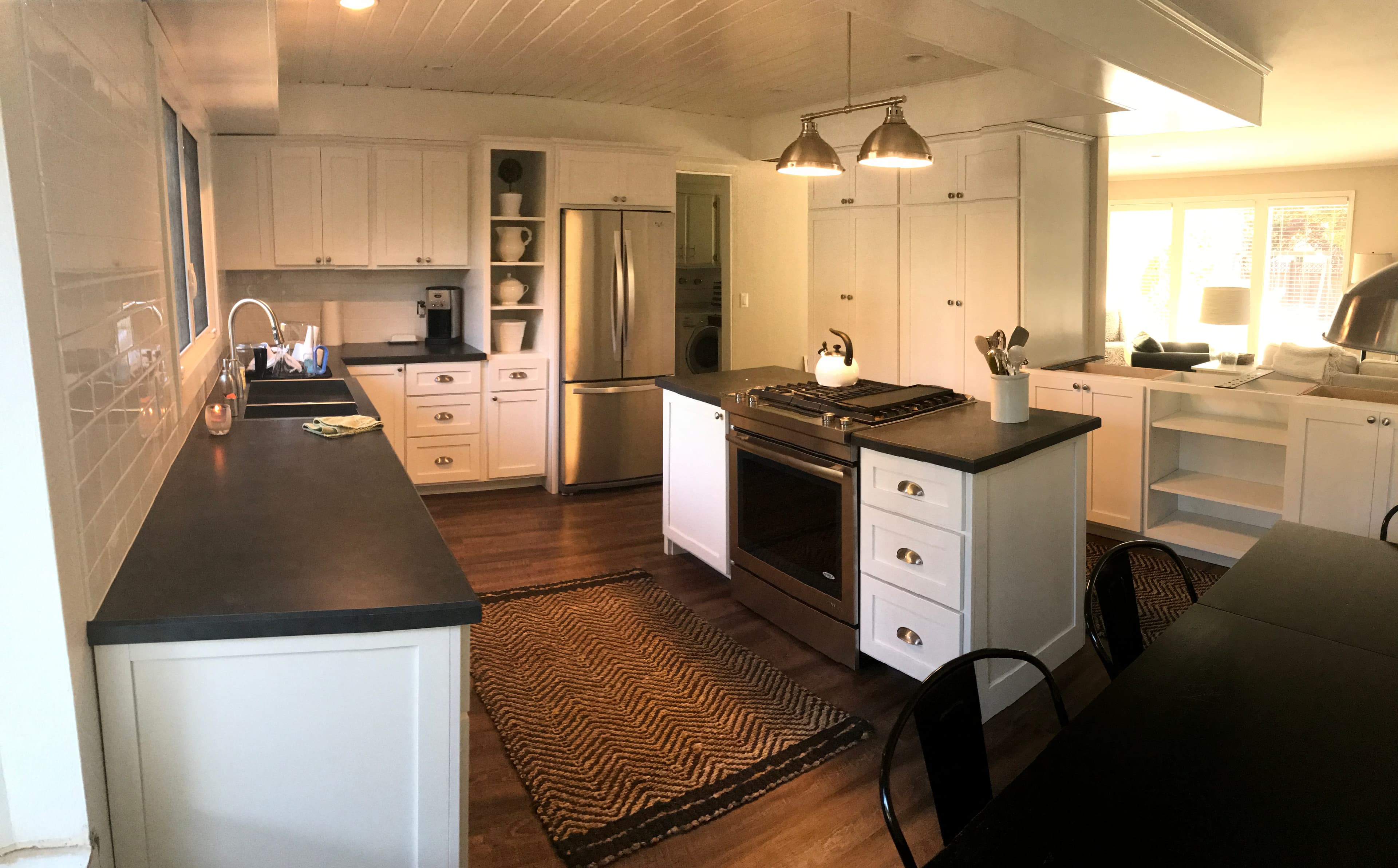White shaker kitchen with a farmhouse sink, custom island, dark counters, and open shelving