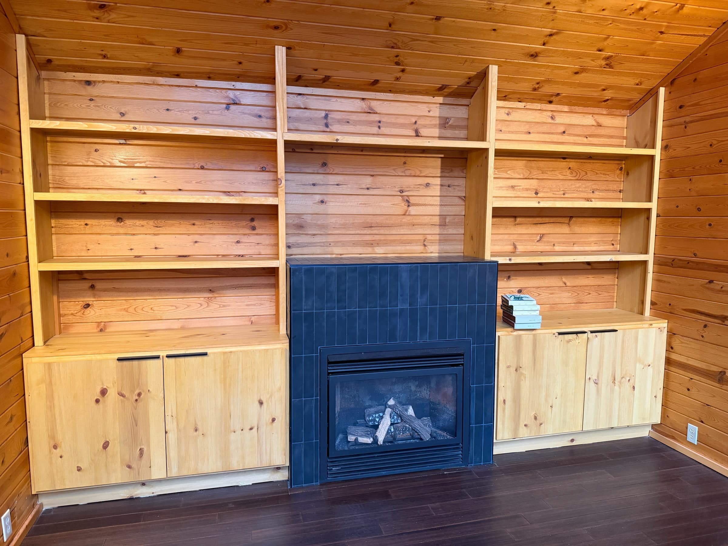 Installed pine shelves and four solid pine cabinet doors around a blue tiled fireplace in a pine-paneled room